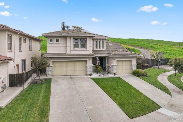 prairie-style home featuring stone siding, stucco siding, concrete driveway, and fence