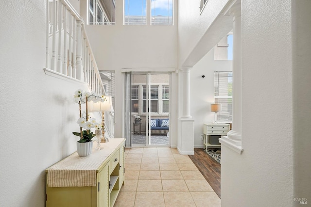 foyer with light tile patterned floors, a wealth of natural light, ornate columns, and a towering ceiling