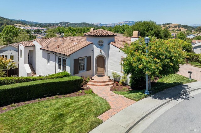 mediterranean / spanish-style home with a front yard, a tiled roof, a mountain view, and stucco siding