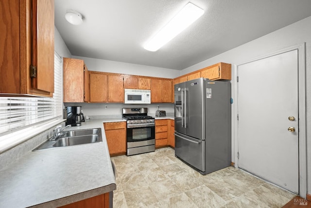 kitchen with brown cabinets, stainless steel appliances, light countertops, and a sink