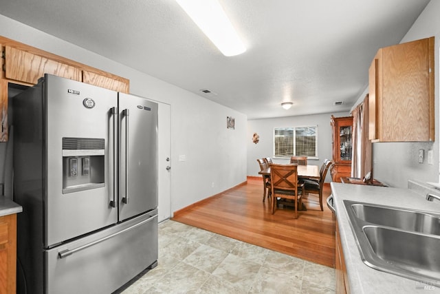 kitchen with a sink, a textured ceiling, stainless steel fridge, light countertops, and baseboards
