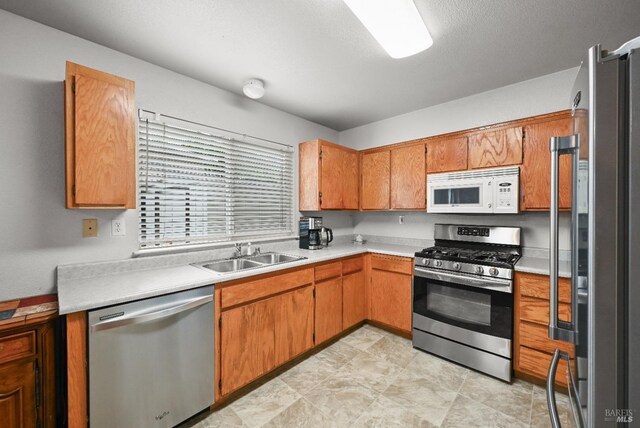 kitchen with light countertops, brown cabinets, appliances with stainless steel finishes, and a sink