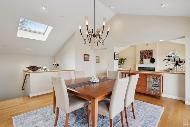 dining room featuring a chandelier, light wood finished floors, a premium fireplace, and lofted ceiling with skylight