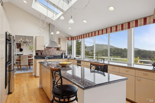kitchen with a mountain view, wall chimney exhaust hood, a sink, a kitchen island with sink, and a skylight