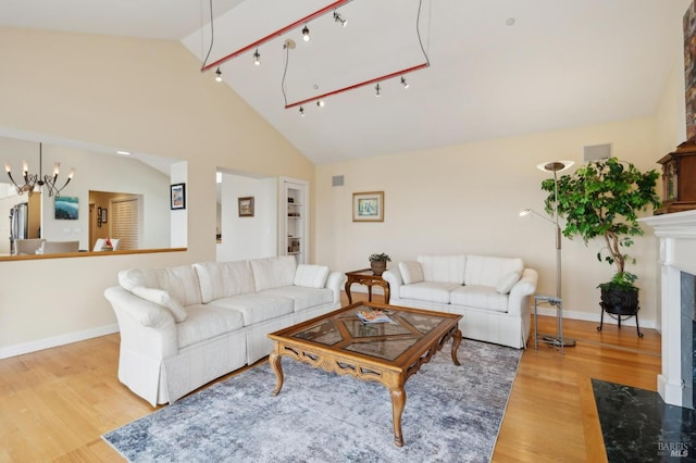 living room featuring baseboards, a chandelier, a fireplace, light wood-style flooring, and lofted ceiling