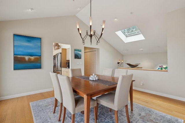 dining room with light wood-style flooring, an inviting chandelier, baseboards, and lofted ceiling with skylight