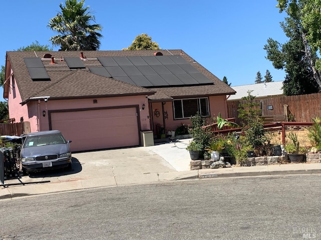 view of front facade featuring concrete driveway, an attached garage, fence, and roof mounted solar panels