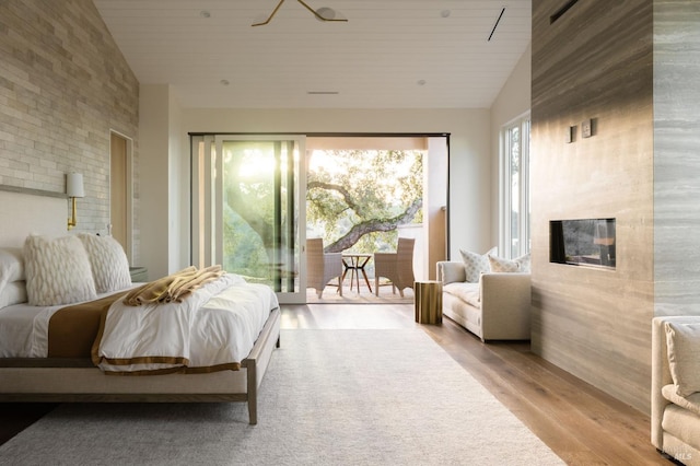 bedroom featuring high vaulted ceiling, a tiled fireplace, access to outside, wood finished floors, and wood ceiling