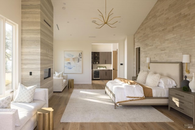 bedroom featuring a high end fireplace, wine cooler, an inviting chandelier, wood finished floors, and high vaulted ceiling