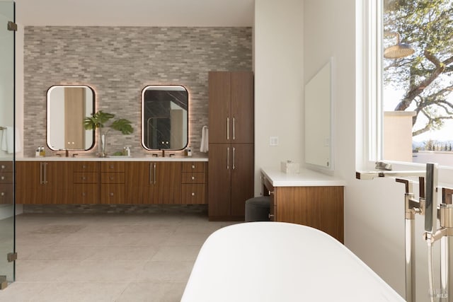 bathroom with double vanity, a freestanding tub, a sink, tile patterned floors, and backsplash