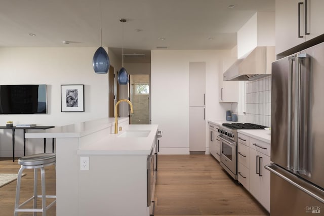 kitchen featuring an island with sink, light countertops, premium appliances, a kitchen breakfast bar, and a sink