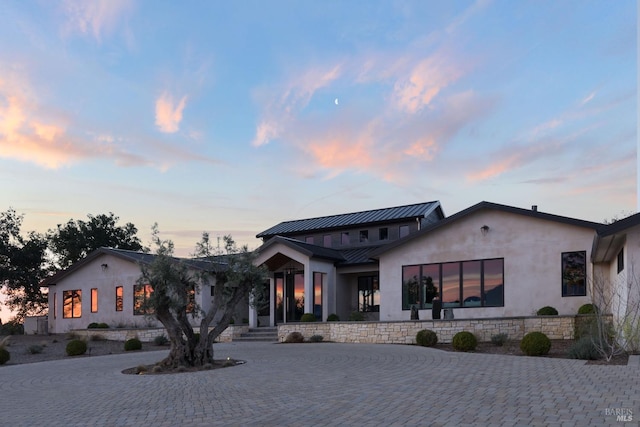 view of front of property featuring stucco siding, a standing seam roof, stone siding, curved driveway, and metal roof