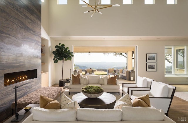 living room featuring a tiled fireplace, a high ceiling, an inviting chandelier, and wood finished floors