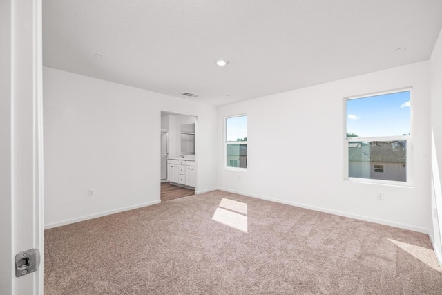 unfurnished bedroom featuring light colored carpet, visible vents, multiple windows, and baseboards