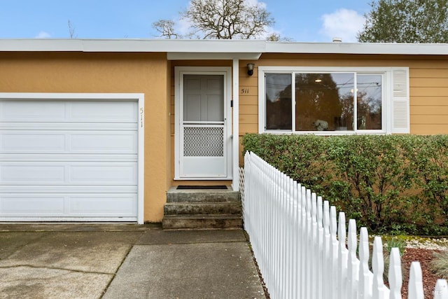 property entrance featuring a garage, driveway, stucco siding, and fence
