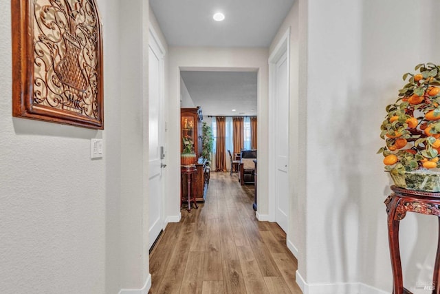 corridor with baseboards, light wood finished floors, and recessed lighting