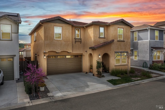 view of front of house with a tiled roof, driveway, fence, an attached garage, and stucco siding