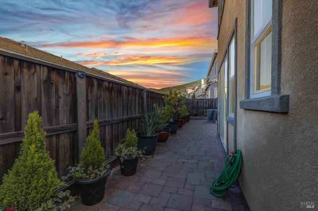 property exterior at dusk with a patio, a fenced backyard, central air condition unit, and stucco siding