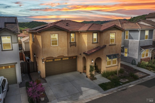 view of front facade with driveway, a tiled roof, an attached garage, fence, and stucco siding