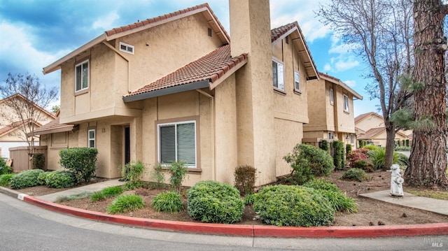 view of side of property with a tile roof, a chimney, and stucco siding