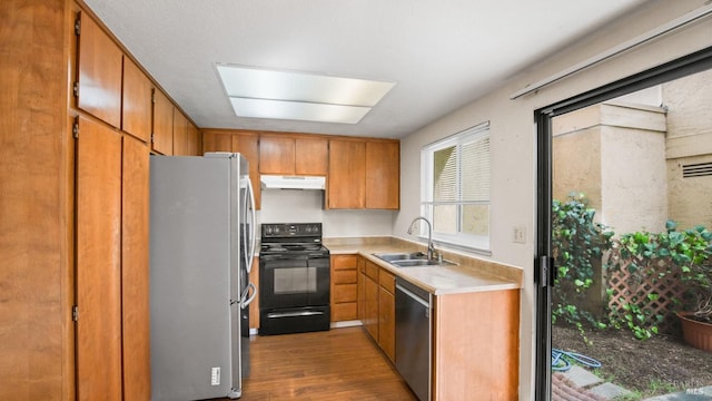 kitchen featuring wood finished floors, a sink, stainless steel appliances, light countertops, and under cabinet range hood