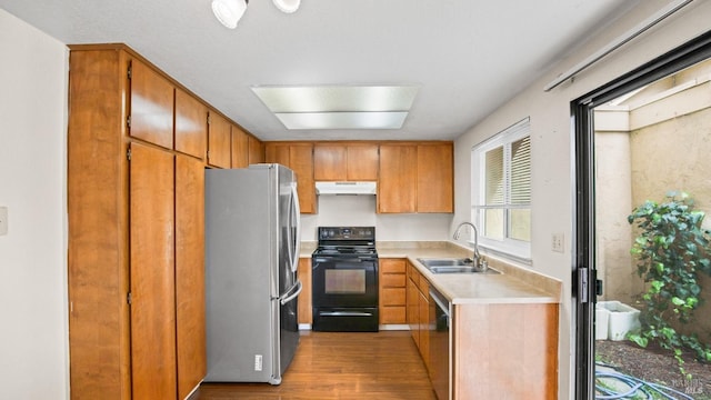 kitchen featuring wood finished floors, a sink, stainless steel appliances, light countertops, and under cabinet range hood