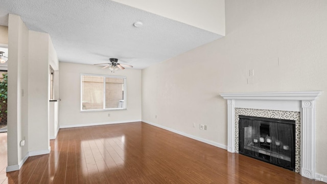 unfurnished living room featuring a ceiling fan, a tiled fireplace, a textured ceiling, wood finished floors, and baseboards