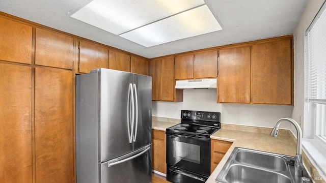 kitchen featuring black / electric stove, freestanding refrigerator, a sink, under cabinet range hood, and brown cabinets