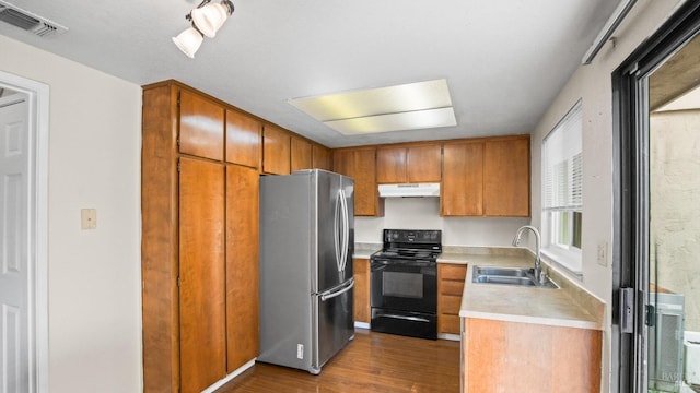 kitchen featuring under cabinet range hood, light countertops, freestanding refrigerator, black electric range oven, and a sink