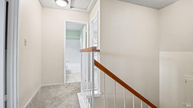hallway featuring baseboards, an upstairs landing, a textured ceiling, and carpet floors
