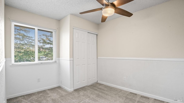 unfurnished bedroom featuring light carpet, a textured ceiling, a closet, baseboards, and ceiling fan