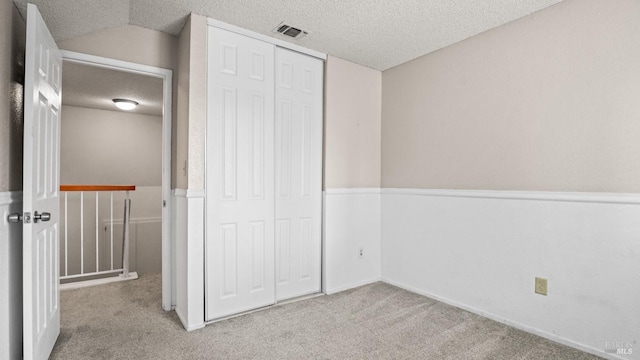 unfurnished bedroom featuring visible vents, vaulted ceiling, carpet floors, a closet, and a textured ceiling