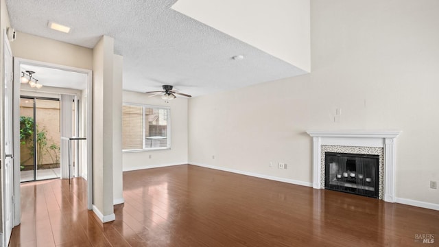 unfurnished living room with dark wood-type flooring, baseboards, a tiled fireplace, a textured ceiling, and a ceiling fan