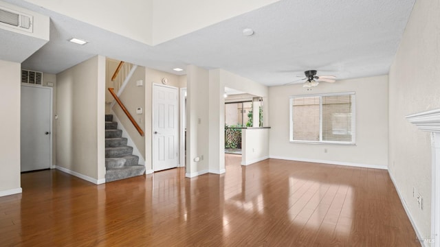 unfurnished living room featuring ceiling fan, visible vents, wood finished floors, and stairs