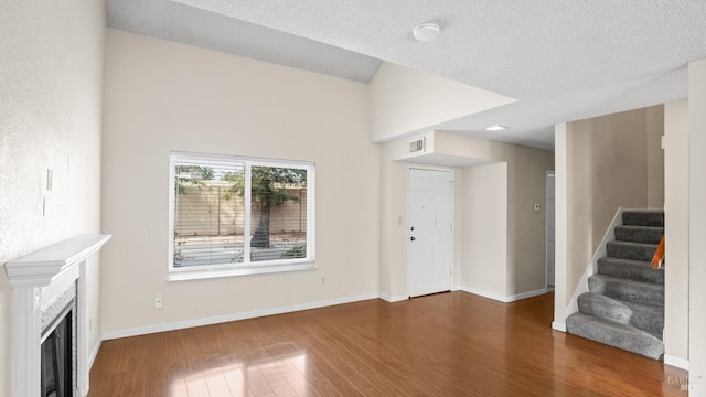 unfurnished living room featuring visible vents, baseboards, stairway, wood finished floors, and a textured ceiling