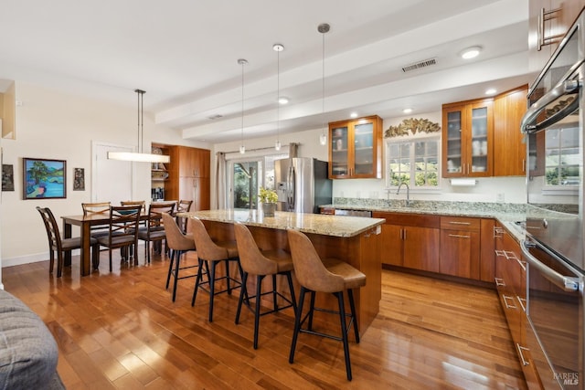 kitchen featuring visible vents, a center island, brown cabinets, appliances with stainless steel finishes, and light wood-style flooring