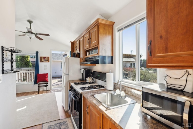 kitchen featuring stainless steel microwave, under cabinet range hood, range with gas stovetop, brown cabinets, and a sink