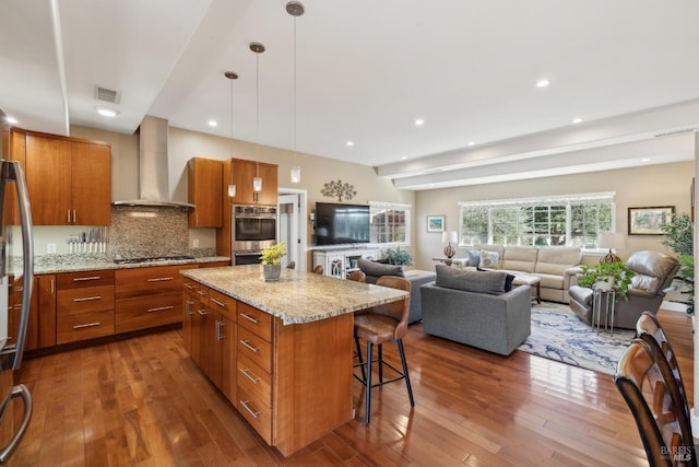 kitchen featuring visible vents, a kitchen bar, wall chimney exhaust hood, and brown cabinetry