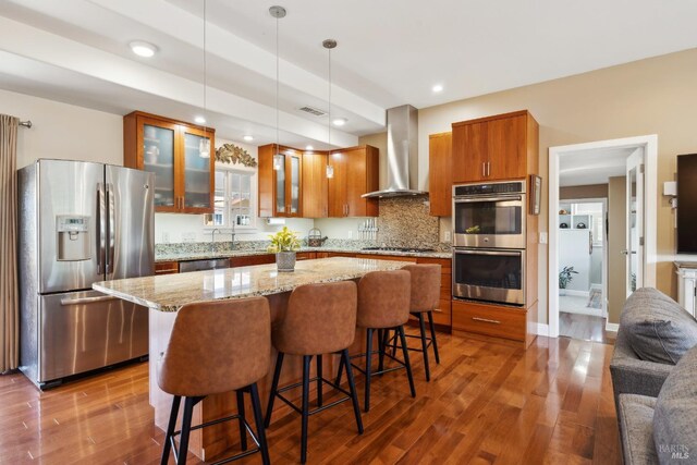 kitchen featuring brown cabinetry, dark wood-style floors, stainless steel appliances, and wall chimney exhaust hood