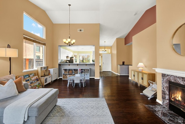 living room featuring high vaulted ceiling, a high end fireplace, an inviting chandelier, a healthy amount of sunlight, and visible vents