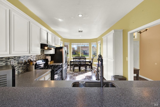 kitchen with dark countertops, tasteful backsplash, white cabinetry, black gas range oven, and under cabinet range hood