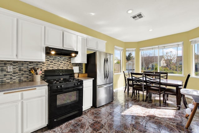 kitchen featuring backsplash, black gas range oven, under cabinet range hood, visible vents, and freestanding refrigerator