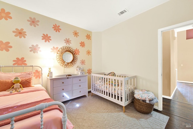 bedroom featuring baseboards, wallpapered walls, wood finished floors, and visible vents
