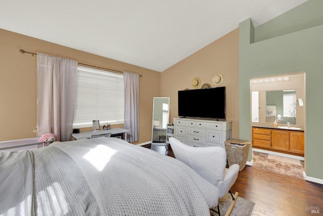 bedroom featuring vaulted ceiling, wood finished floors, multiple windows, baseboards, and ensuite bath