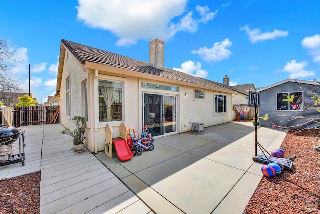 rear view of property featuring a chimney, fence, a patio, stucco siding, and a wooden deck