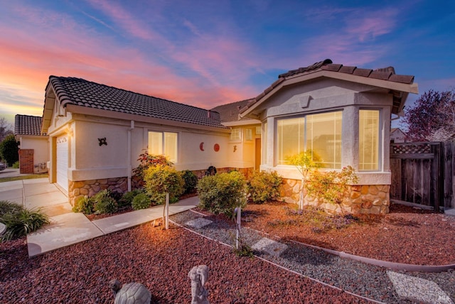 view of front of property featuring an attached garage, fence, stone siding, and a tiled roof
