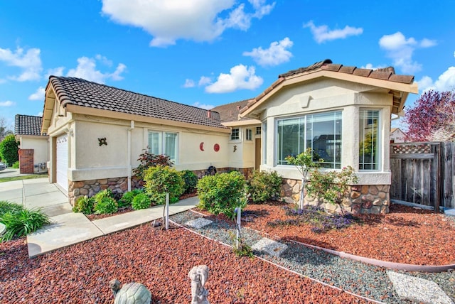 view of front of home featuring fence, a tiled roof, stucco siding, an attached garage, and stone siding