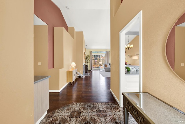 corridor featuring baseboards, a chandelier, and dark wood-style floors