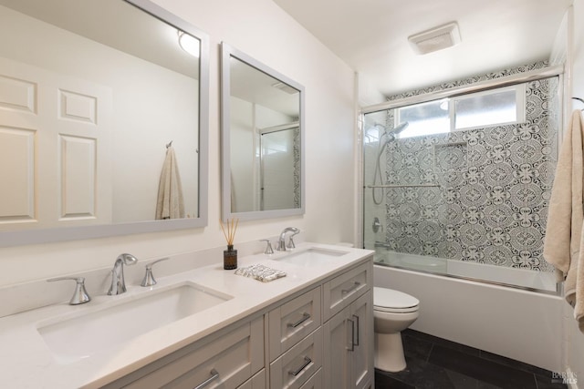 bathroom featuring combined bath / shower with glass door, double vanity, toilet, and a sink