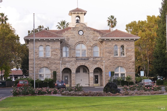 view of front facade with a front lawn, stone siding, and a tile roof